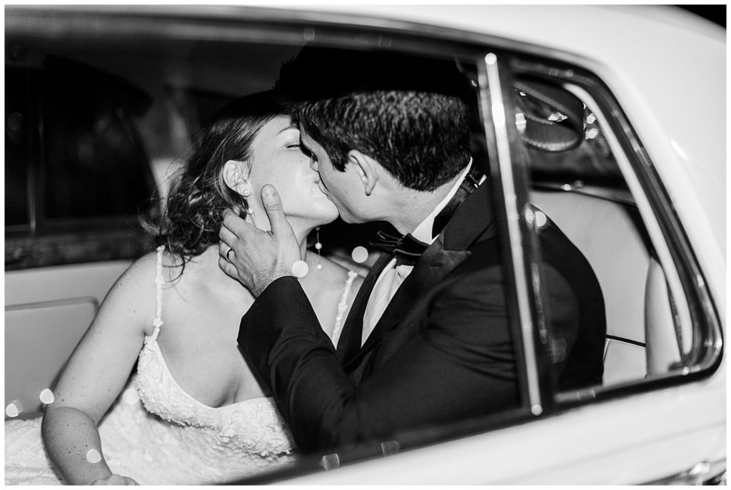 A bride and groom kiss in the back of a car. 