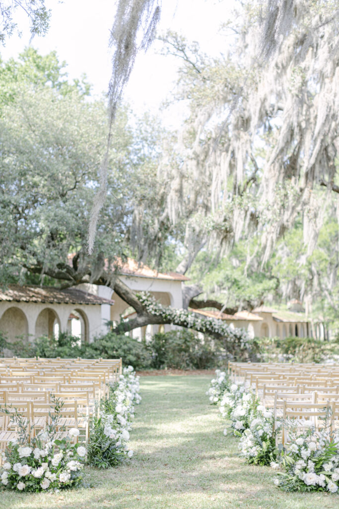 Chairs set up for a garden wedding with sandstone archways behind a hanging oak tree.