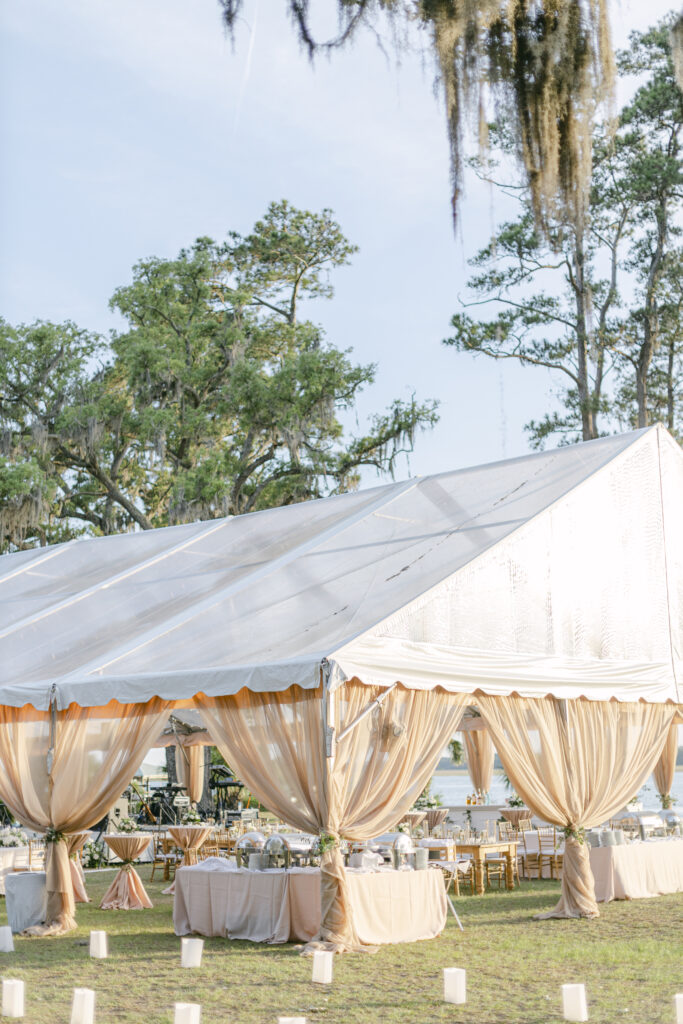 Large Peach tent with tables and chairs beneath it backdropped by water.