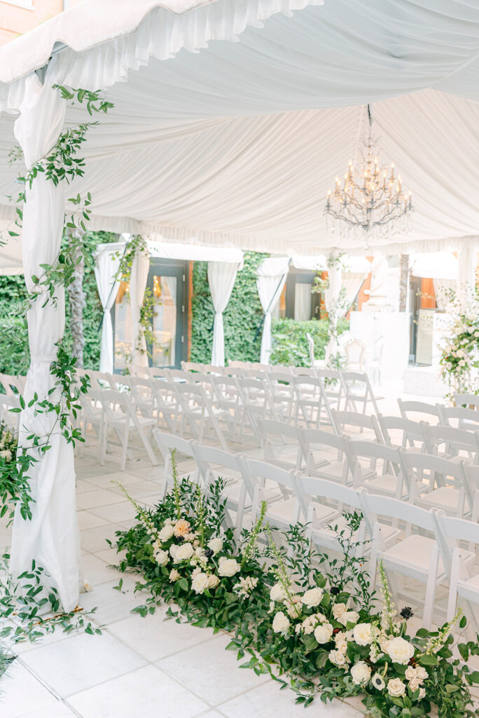 A white-themed tent with white chairs and florals.