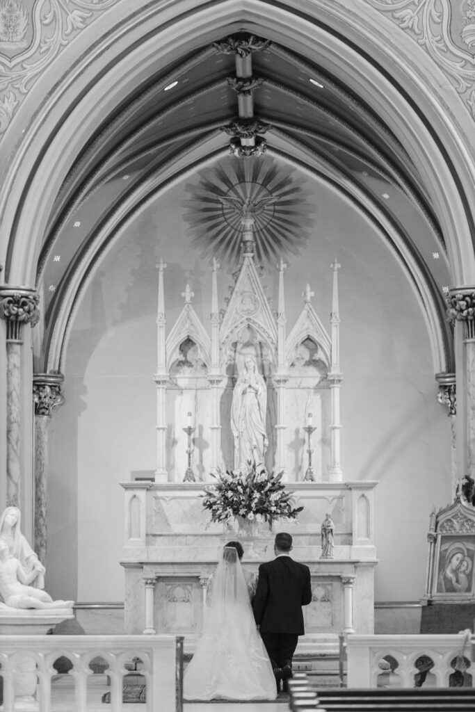 A bride and groom kneel before the statue of Mary.