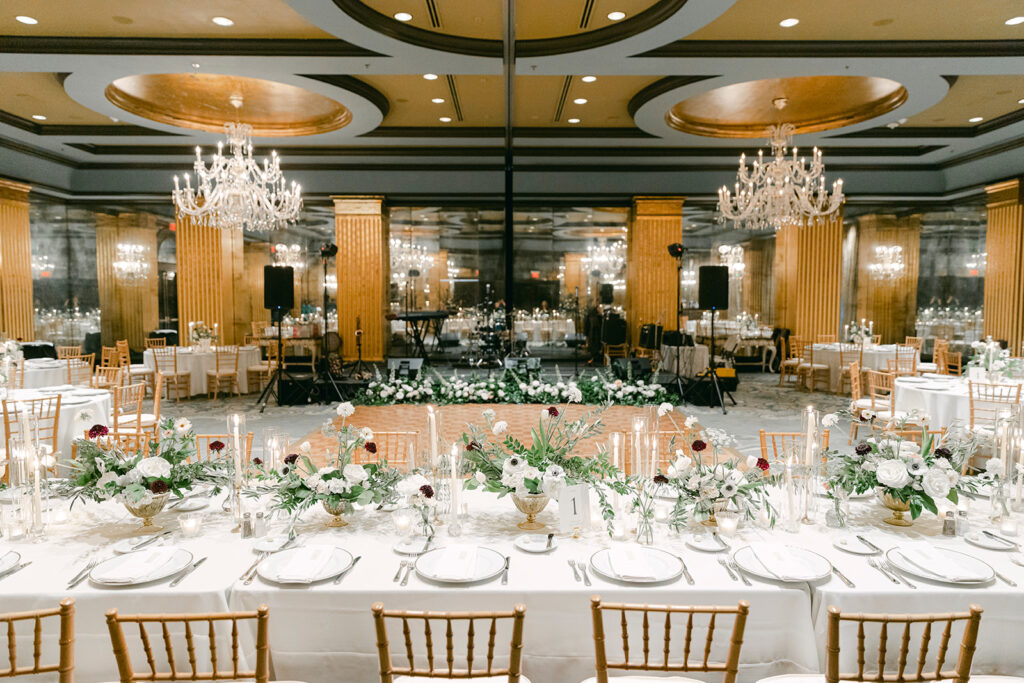 A gold and black ballroom with white tables and brown chairs.