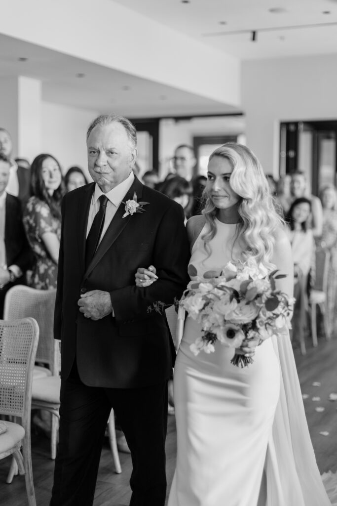 A bride is lead by her father as she walks down the aisle.