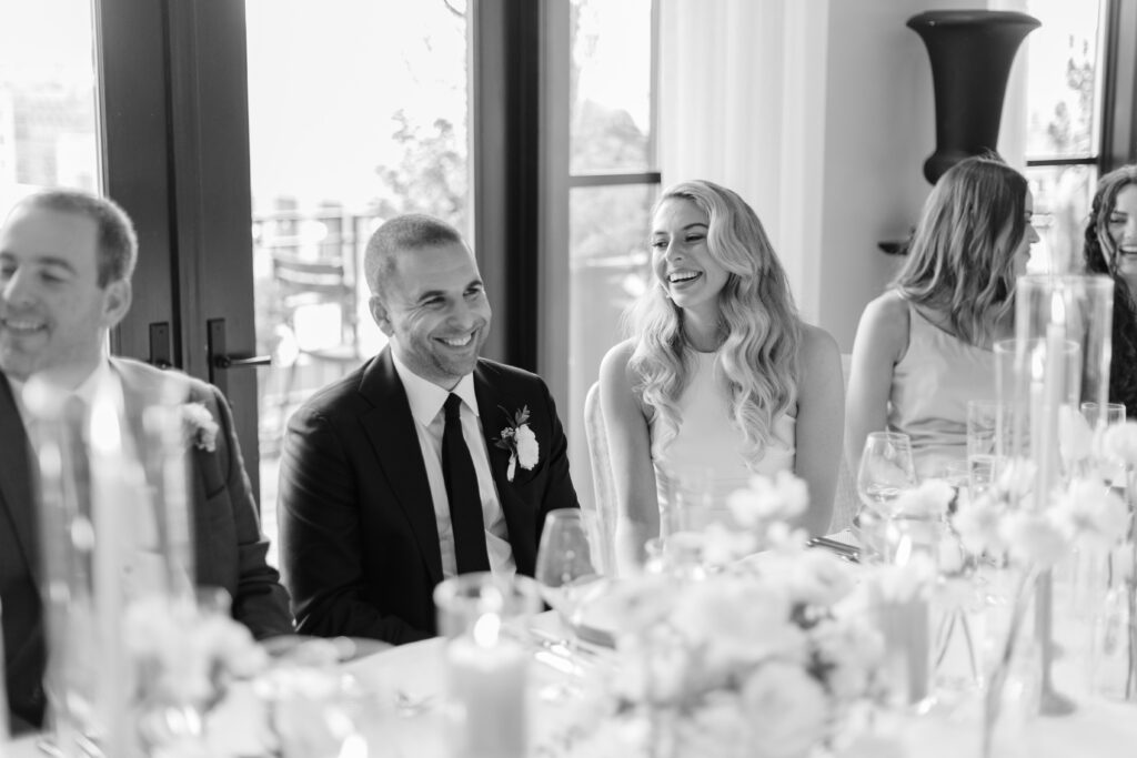 A bride smiles at her groom as they sit at a table. 