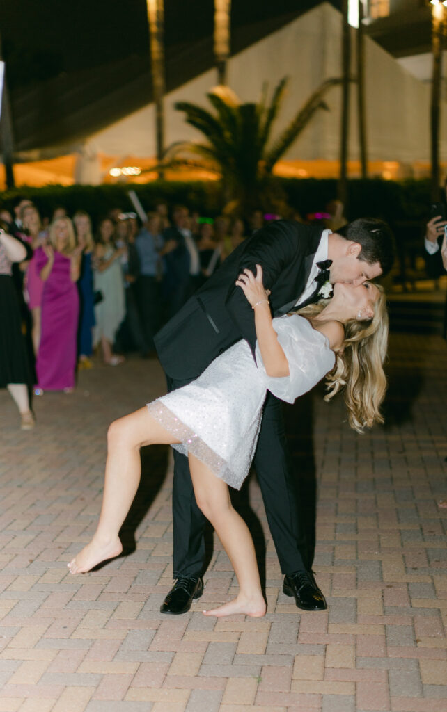 A groom dips his barefoot bride and kisses her. 