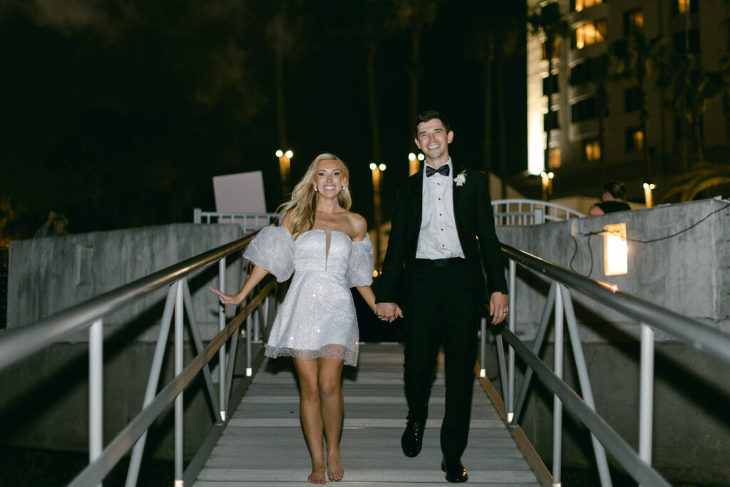 A bride and groom walk down a gangplank at night. 