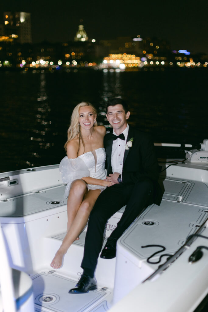 A bride and groom sitting on the bow of a boat. 