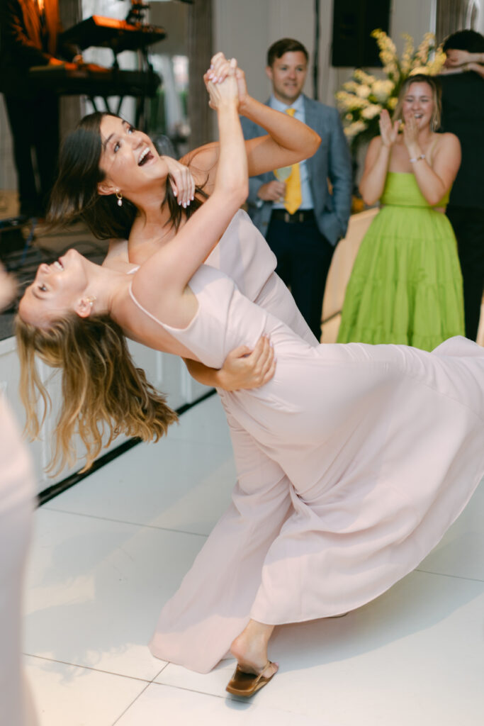 Two female guests dance at a wedding. 
