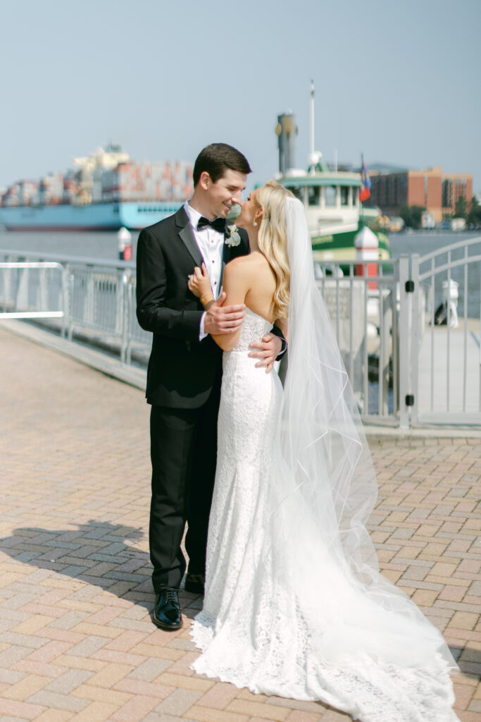 A bride and groom nuzzle in front of a tug boat. 