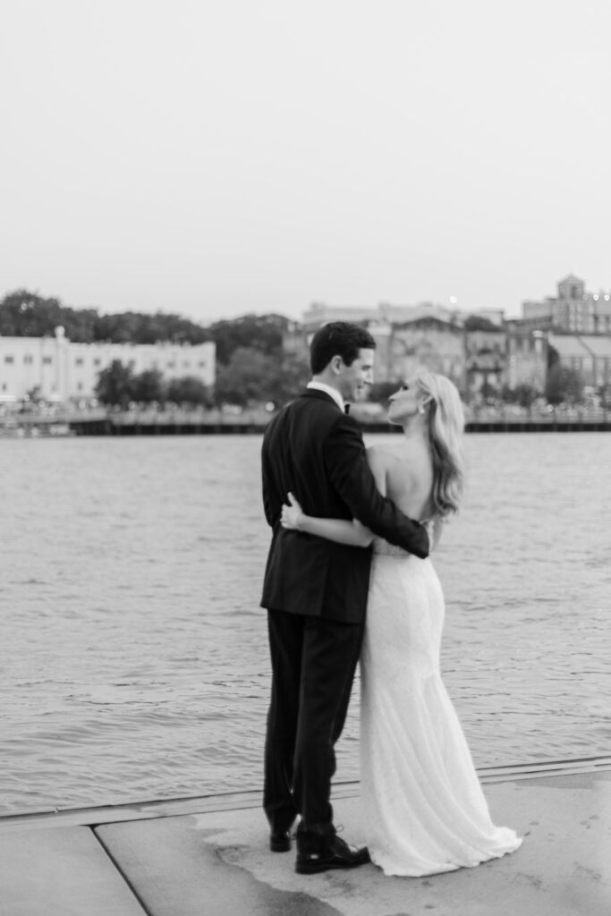 A bride and groom stare longingly at one another overlooking the water. 