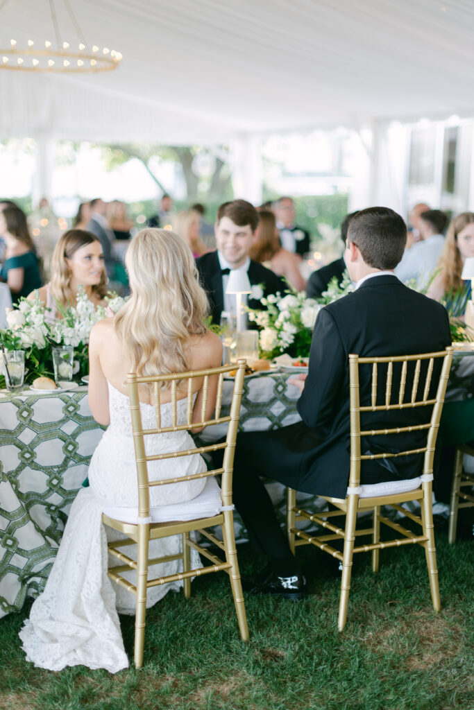 A bride and groom sit in chairs with guests. 