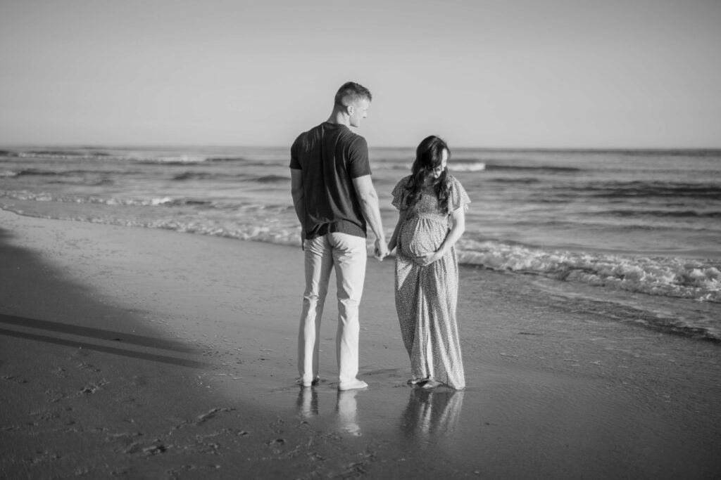 A mother and father stand on the beach looking at the water. 