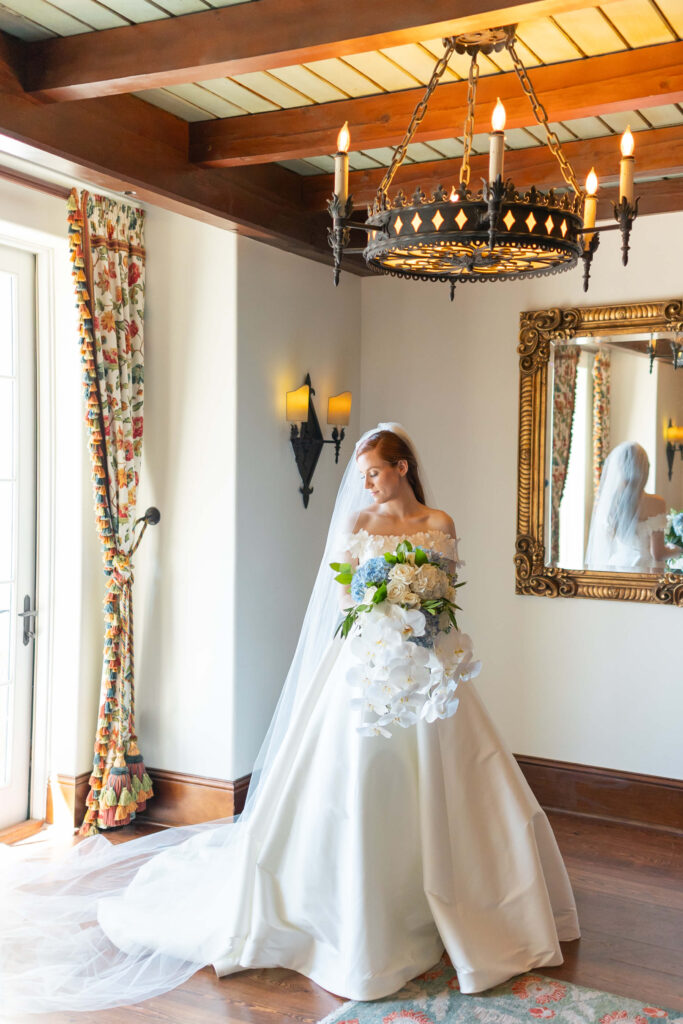 A bride holds a bouquet of orchids while standing under a chandelier. 
