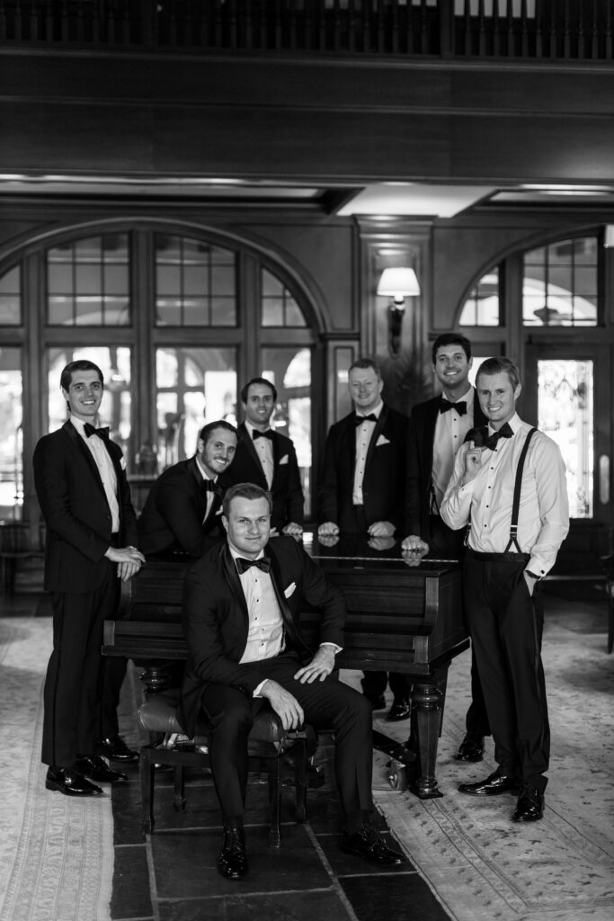 A groom sits at a piano surrounded by his best men. 