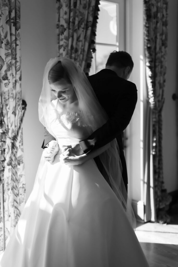 A bride and groom stand back to back while reading letters to each other. 