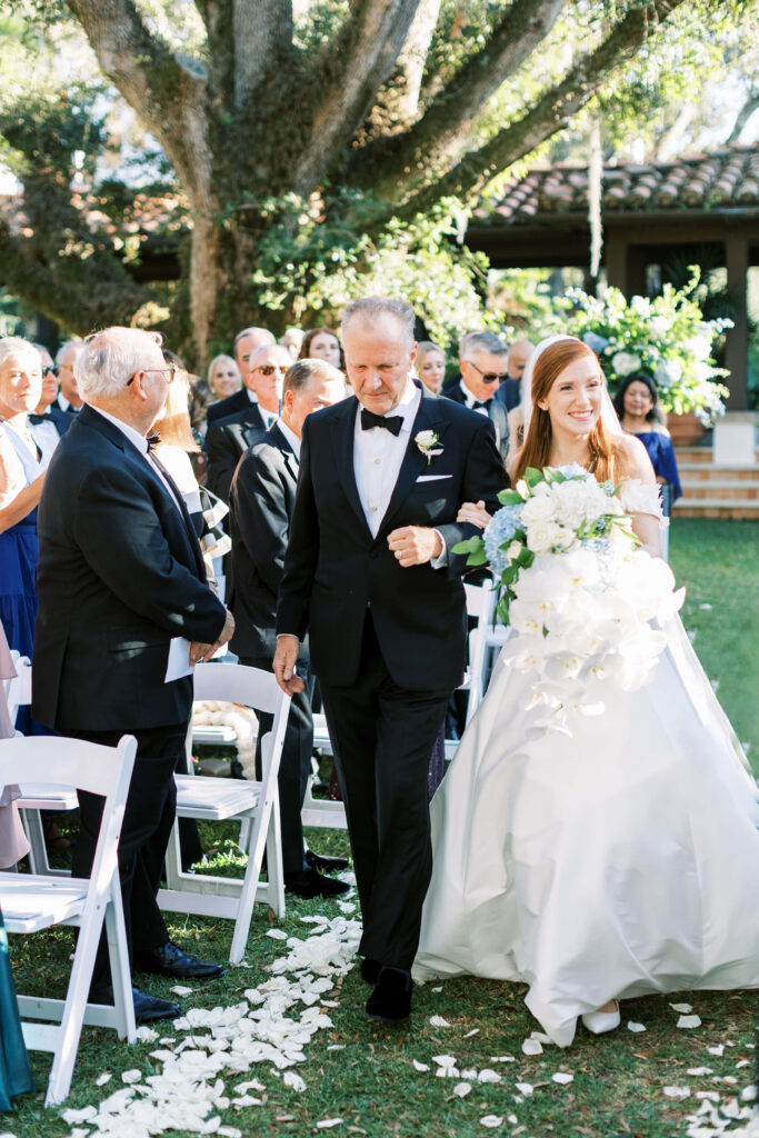 A bride smiles while walking down the aisle with her father. 