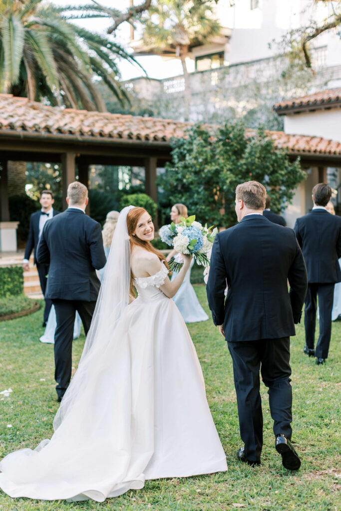 A bride smiles over her shoulder while walking with her groom.