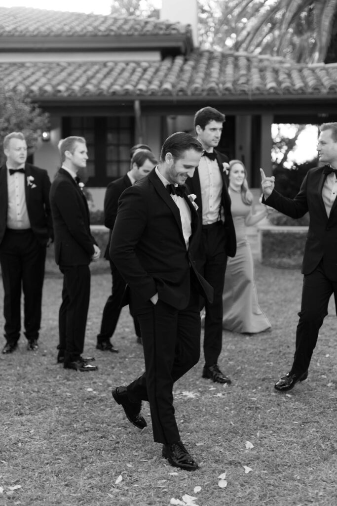 A groomsman smiles while walking with his hands in his pockets. 