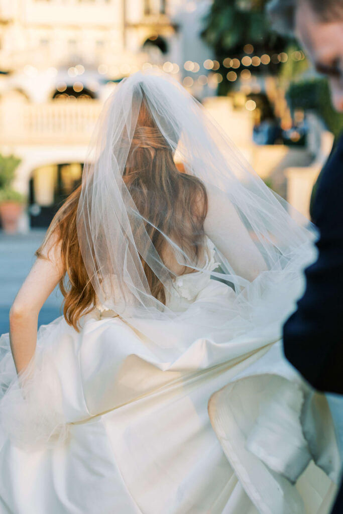 A bride as seen from the back, holding her dress up as she walks. 