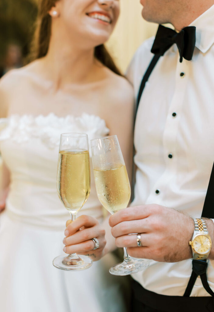 A bride and groom clink their champagne glasses. 
