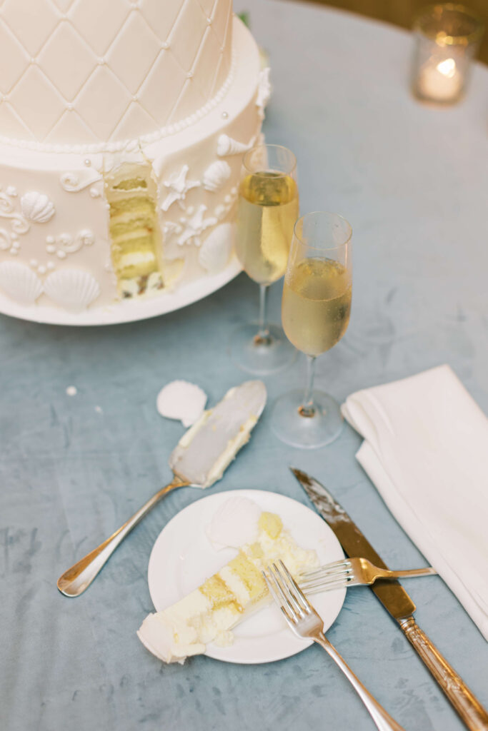 A cake with a slice cut out of it and two glasses of champagne sit on a table. 