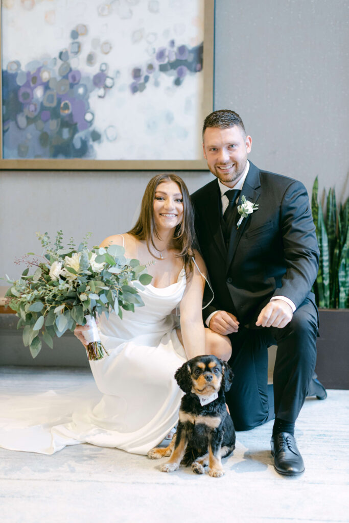 A bride and groom kneel with their puppy. 