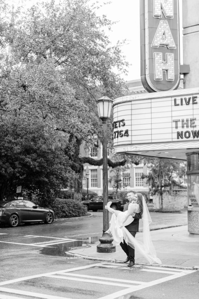 A groom carries his bride across the street at the Savannah Theatre. 