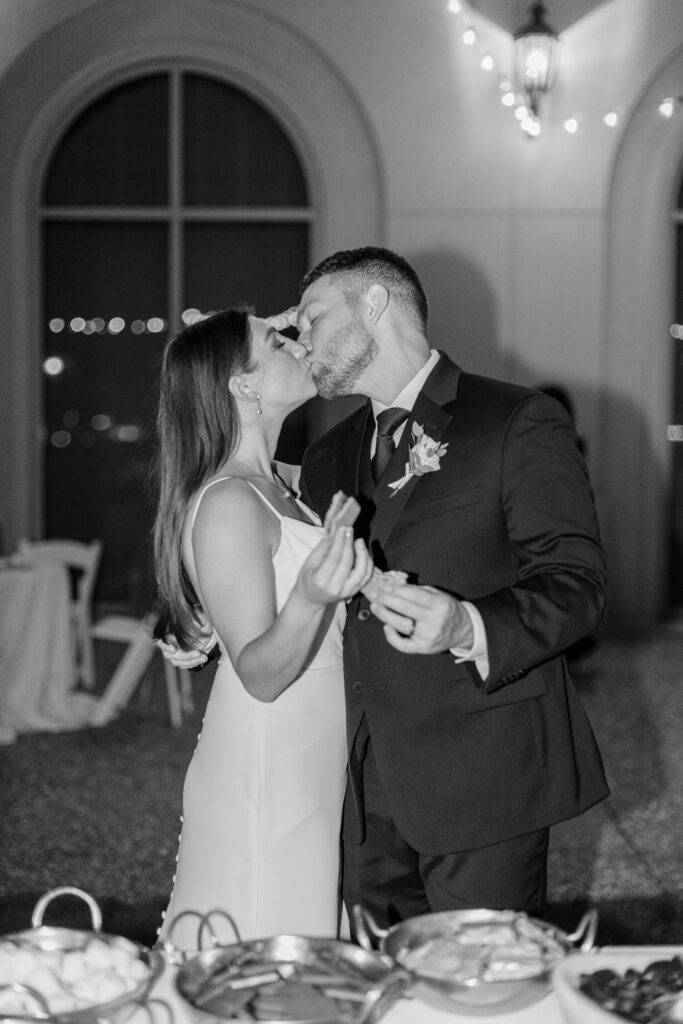 A bride and groom kiss while holding s'mores. 